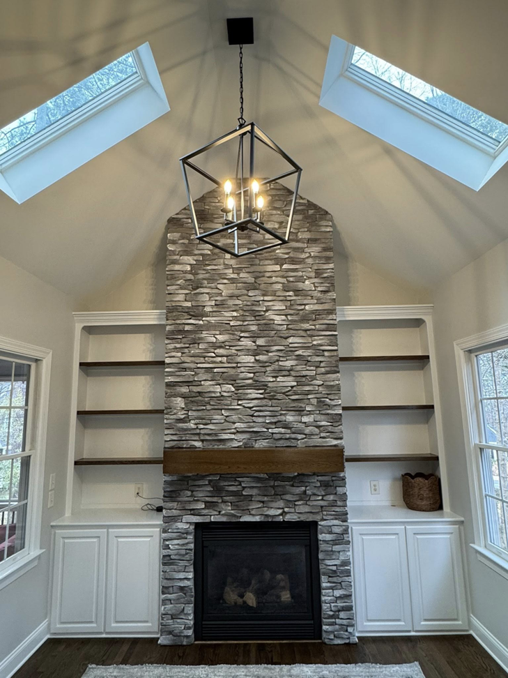 A newly installed stone fireplace with custom built-in shelves and a modern chandelier by Branch Home Improvement LLC in Raleigh, NC.