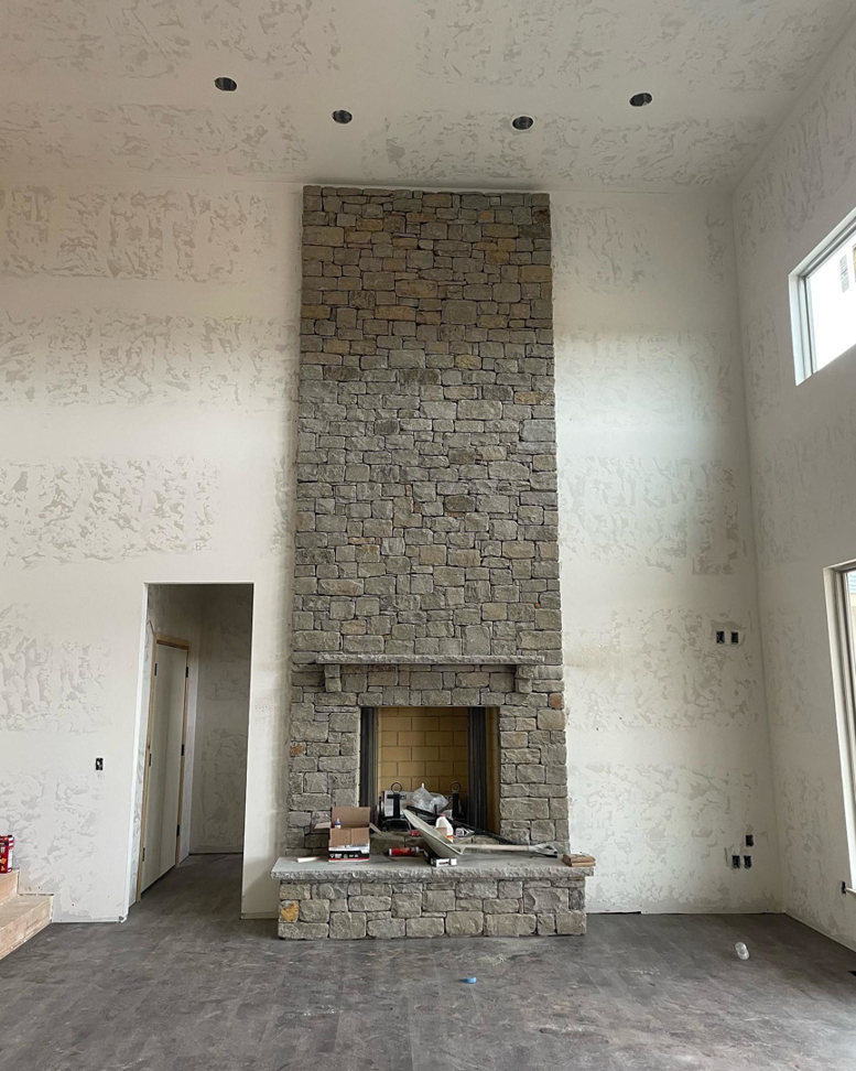 A tall stone fireplace being installed in a room under renovation by Bryan Lee Builds in Oklahoma City, OK.