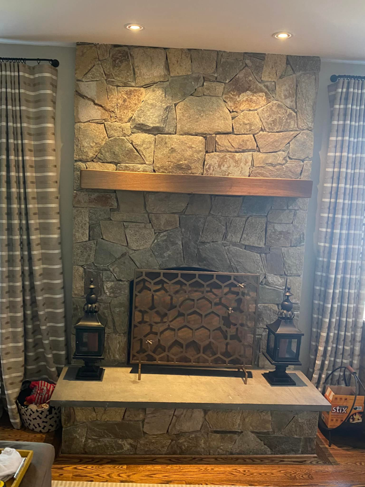 A beautifully remodeled stone fireplace with a wooden mantel and hearth by Andyman,LLC in Fredrick, MD.