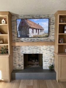 A newly installed stone veneer fireplace with a wooden mantel and mounted TV by Titan Handyman Services in Lewes, DE