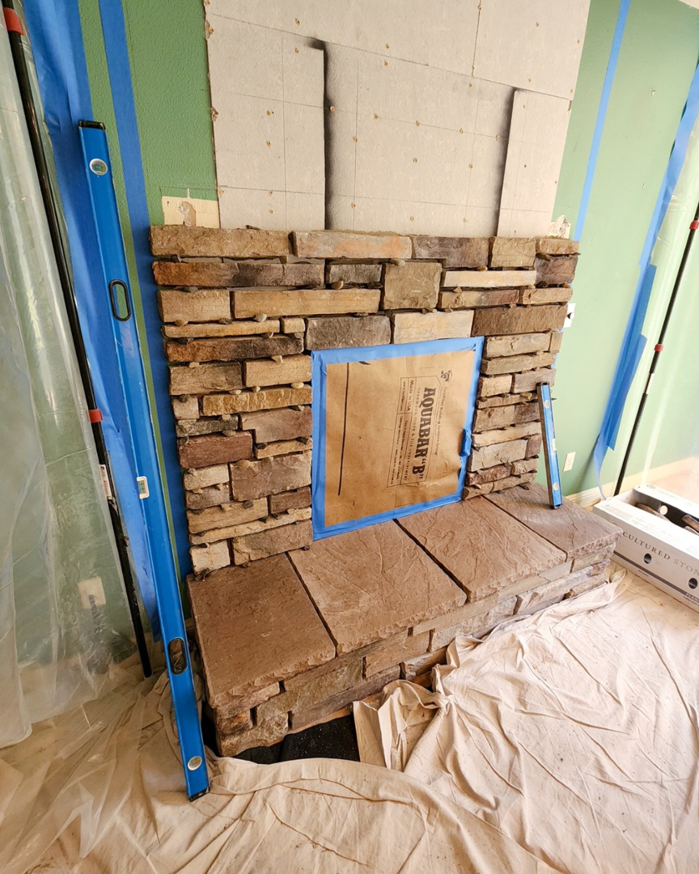 Stone veneer installation in progress on a fireplace, with the opening protected, by Portland Fireplace and Chimney Inc. in Portland, OR.