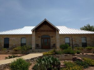A beautiful single-story stone house featuring a new white metal roof and updated landscaping, completed by Custer Remodeling in Plano, TX.