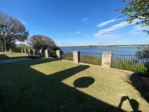 An outdoor area with stone pillars and black metal fencing providing a secure lake view, installed by Falls Contracting, LLC in Raleigh, NC.