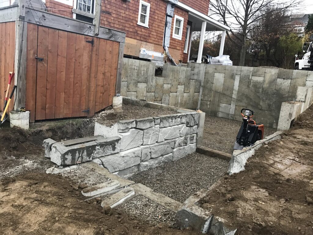 Construction of a new stone retaining wall next to a building by Solimini Excavation and Utility in Freetown, MA