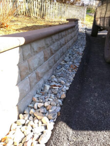 A newly constructed stone retaining wall alongside a driveway with decorative gravel, built by Landscape By Today in Bowie, MD.
