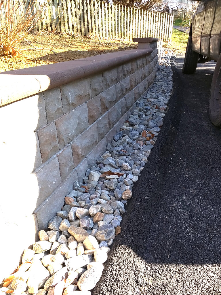 A newly constructed stone retaining wall alongside a driveway with decorative gravel, built by Landscape By Today in Bowie, MD.