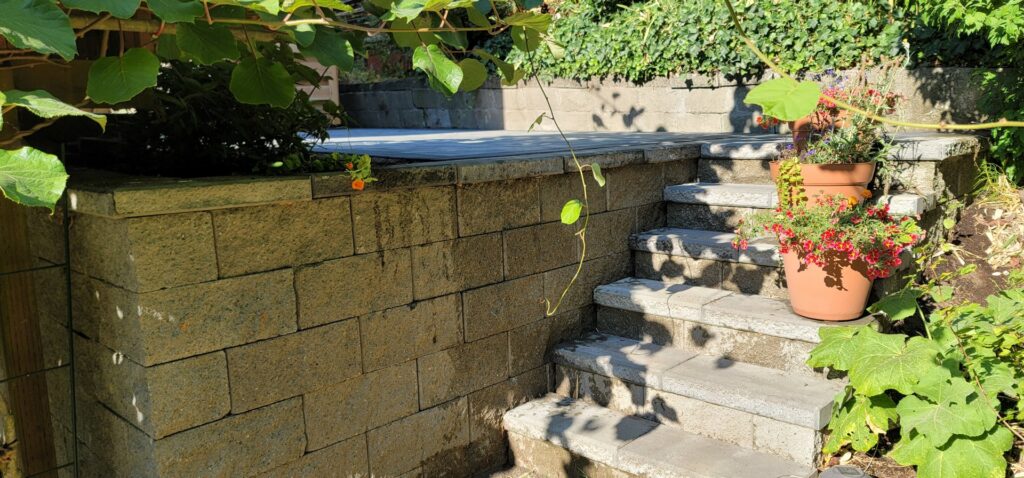 A sturdy stone retaining wall with integrated steps and potted plants by LMS Landscapes & Fence services in Auburn, WA.