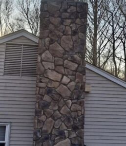 A newly installed stone veneer chimney on the side of a house by Mincho Contractor LLC in Jersey City, NJ