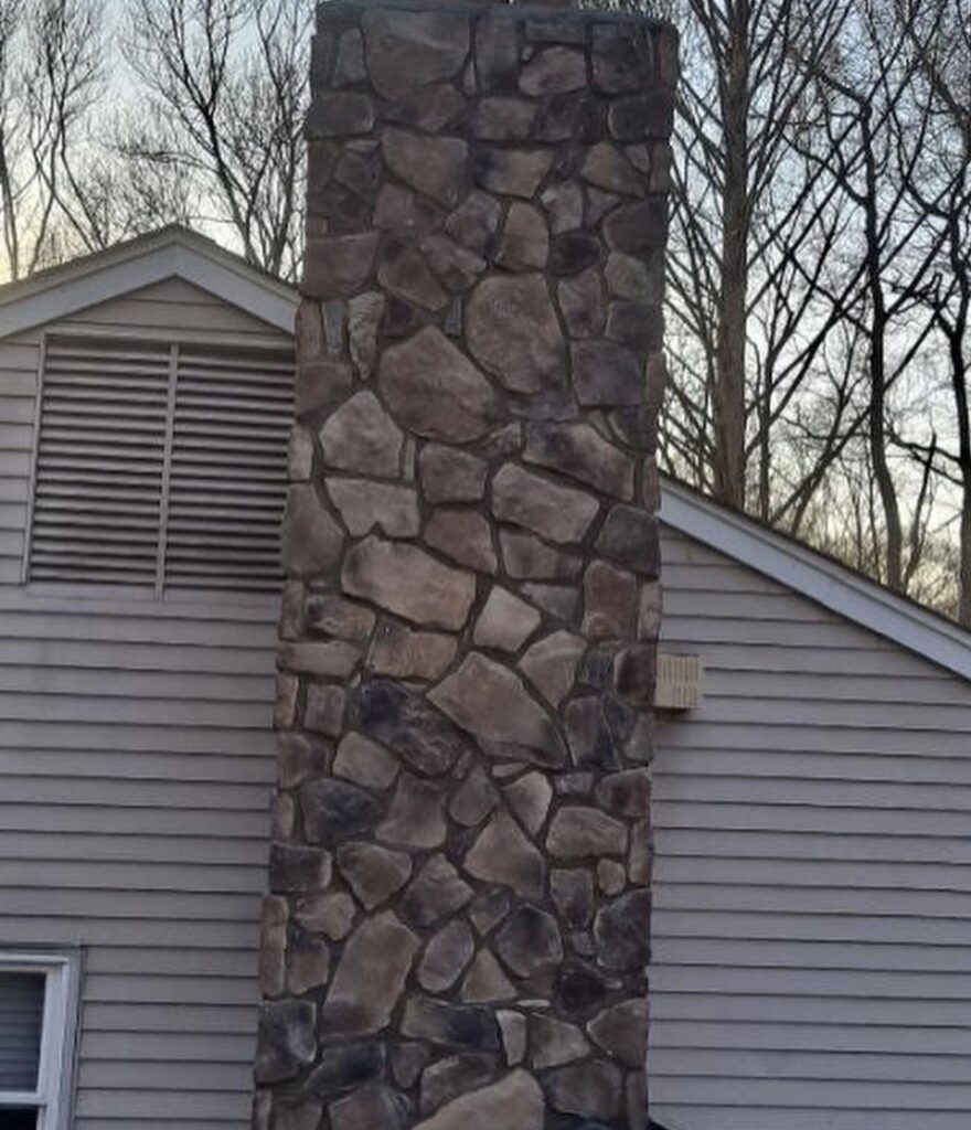 A newly installed stone veneer chimney on the side of a house by Mincho Contractor LLC in Jersey City, NJ