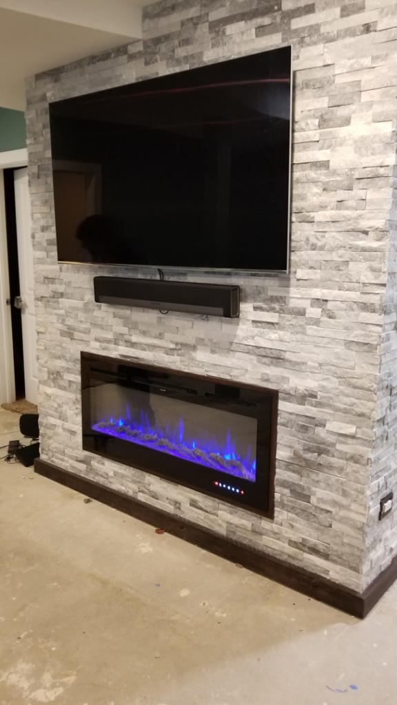 A modern stone veneer fireplace and TV wall installation completed by Quality Home Improvement in Pulaski, Chicago, IL.