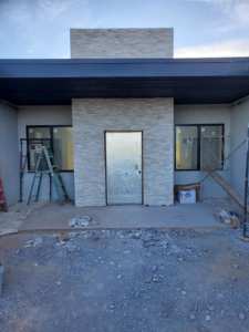 Stone veneer installation in progress on the exterior wall of a home with ladders and materials by AV Handyman Services in Rio Rancho, NM.