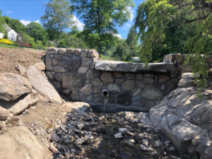 A newly constructed stone wall and bridge with a drainage pipe over a stream by USA Contractors in Danbury, CT.