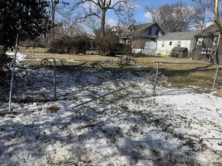 A backyard with fallen tree branches and a broken chain-link fence, showing storm damage cleanup by Grounds and Tree Care in Nashville, TN.