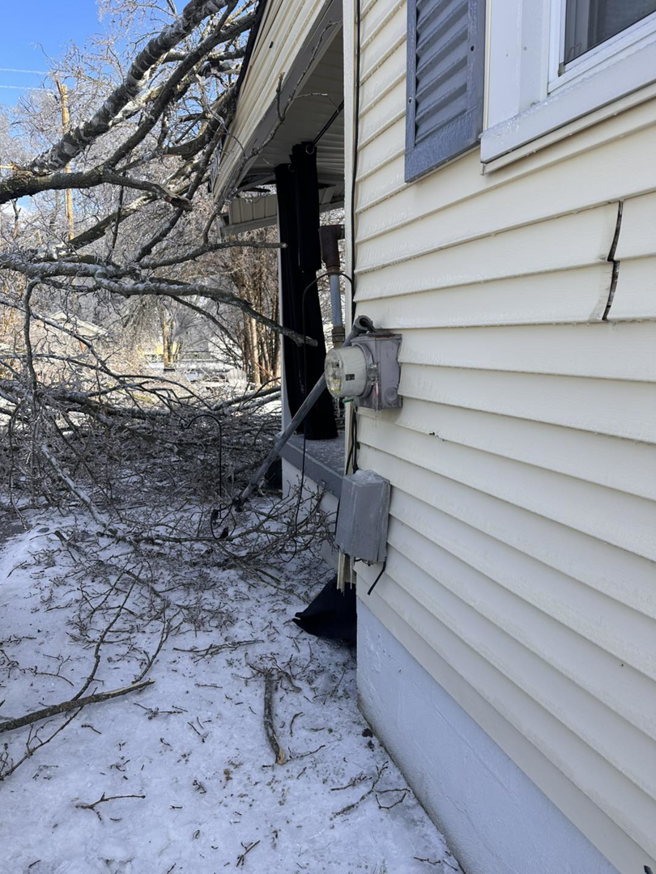 Storm damage with broken branches and cracked siding near an electrical meter, showing repair work by HHS Contractors in Providence Village, TX.