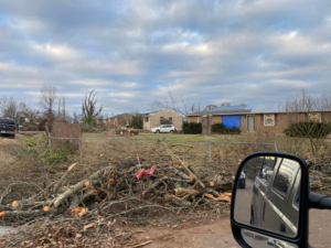 Storm damage aftermath with a blue tarp on a roof and debris pile by Azure Construction in Clarksville, TN