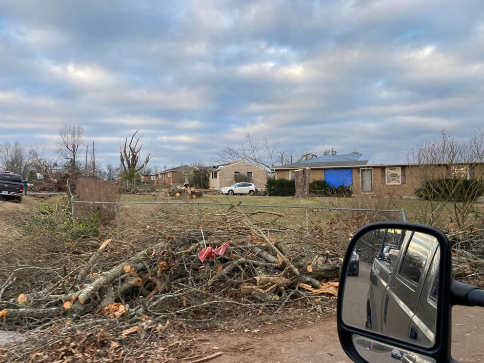 Storm damage aftermath with a blue tarp on a roof and debris pile by Azure Construction in Clarksville, TN