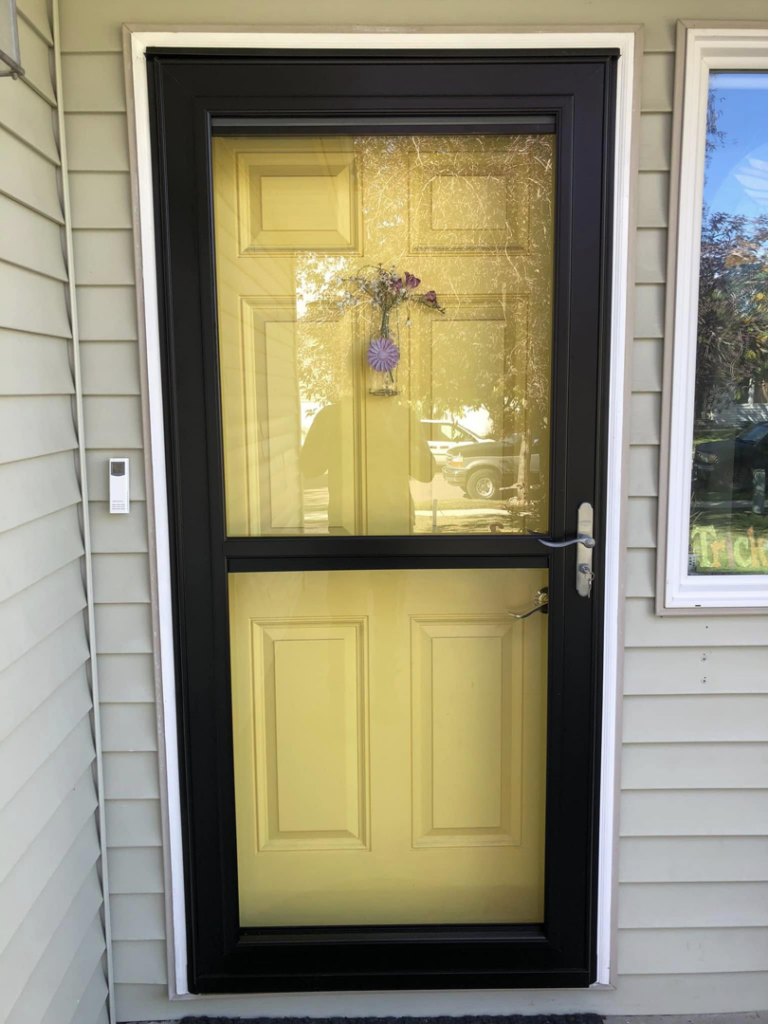 New black storm door installed over a yellow front door by Blue Heron Property Care LLC in Kalispell, MT