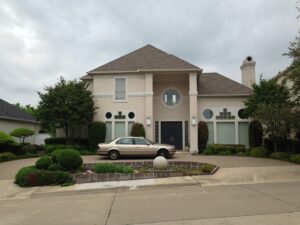 A large, elegant stucco home with a dark roof and distinctive circular windows, showcasing exterior work by Custer Remodeling in Plano, TX.