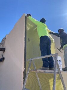 Workers applying stucco mesh to a building wall as part of a project by Old Pueblo Stucco, Inc. in Tucson, AZ