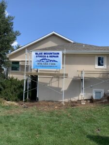 Scaffolding set up for stucco repair on a house, with a Blue Mountain Stucco Repair banner in Greeley, CO