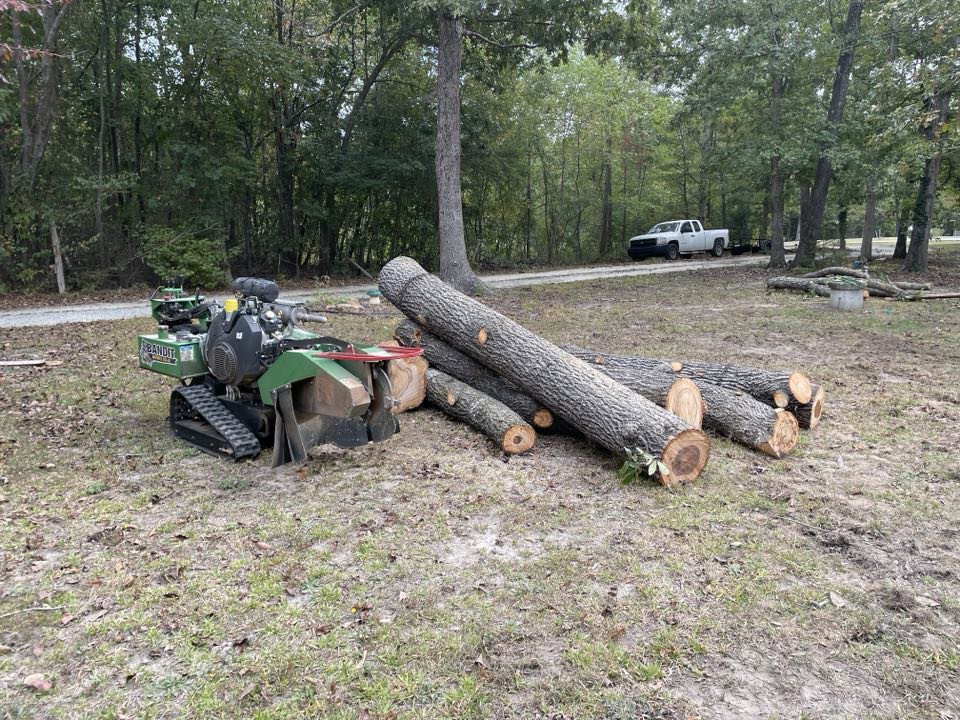 A stump grinder next to a pile of logs, showcasing tree service equipment from Triad Tree Removal LLC in Greensboro, NC.