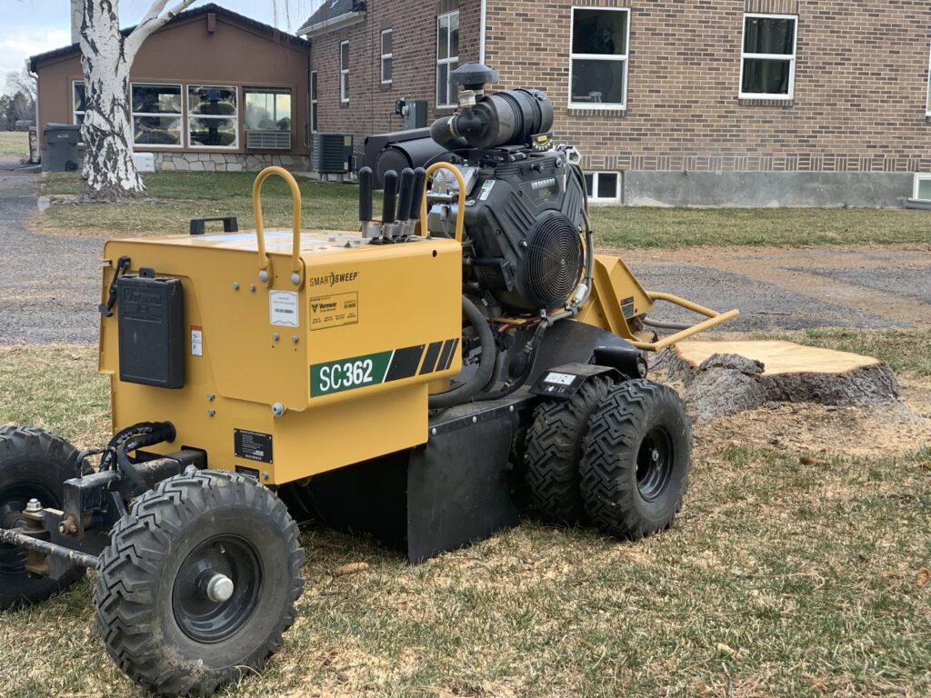 A professional stump grinder machine positioned next to a tree stump for removal by Idaho Stump Grinding in Twin Falls, ID.