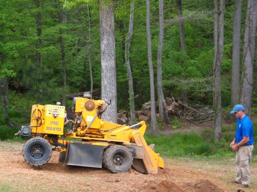 A yellow stump grinder machine operated by Sharp Tree Service in a wooded area in Cumming, GA.