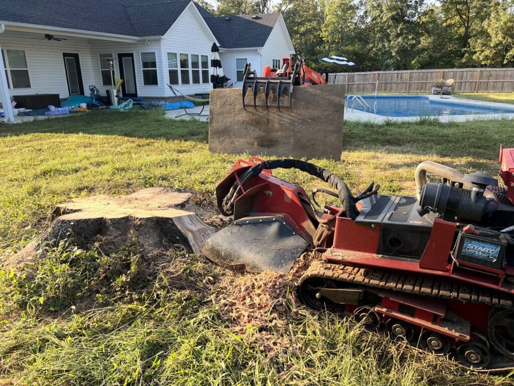 A stump grinder removing a large tree stump next to a residential pool for Liberty Tree in Fort Smith, AR.