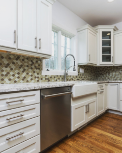 A stylish kitchen featuring white cabinets, a farmhouse sink, and a mosaic tile backsplash, completed by Charlew Builders in Schenectady, NY.