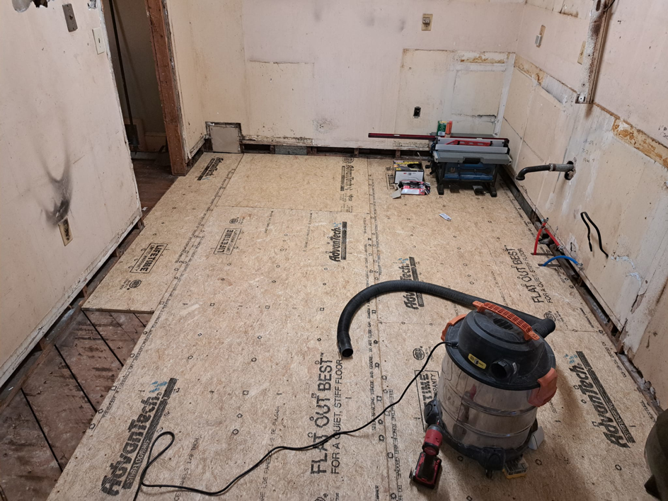 Subfloor installation in a room with a shop vacuum and table saw, by Vest Home Services LLC in Greenville, SC.