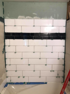White subway tiles with a black accent stripe being installed on a bathroom wall by Ken Sweeney Property Solutions in Knoxville, TN