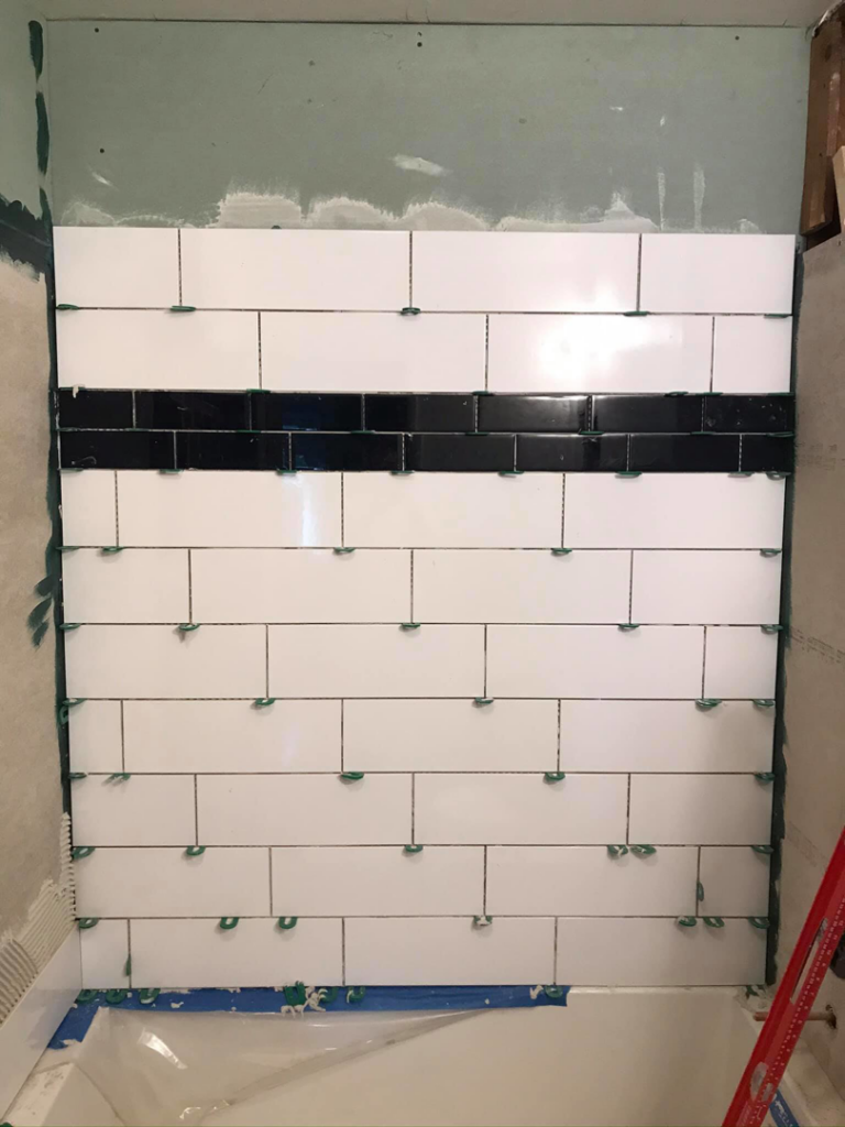 White subway tiles with a black accent stripe being installed on a bathroom wall by Ken Sweeney Property Solutions in Knoxville, TN