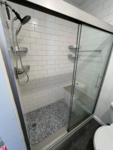 A renovated shower with white subway tiles, glass sliding door, and built-in bench by Roempagel Renovations LLC in South Bend, IN.