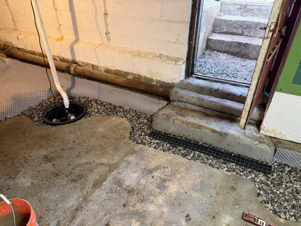A basement floor showing a sump pump pit, drainage system, and gravel fill installed by B-Dry System of New England in North Billerica, MA.