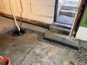 A basement floor showing a sump pump pit, drainage system, and gravel fill installed by B-Dry System of New England in North Billerica, MA.