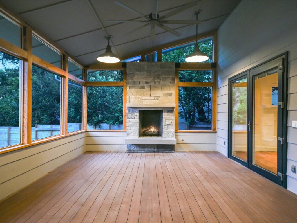 A bright sunroom addition with a cozy stone fireplace and large windows by Transformations Custom Build in Austin, TX