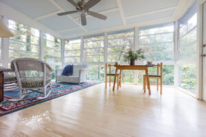 A bright sunroom with large windows, a ceiling fan, and comfortable wicker furniture, a project by Paradise Found Construction in Cary, NC.