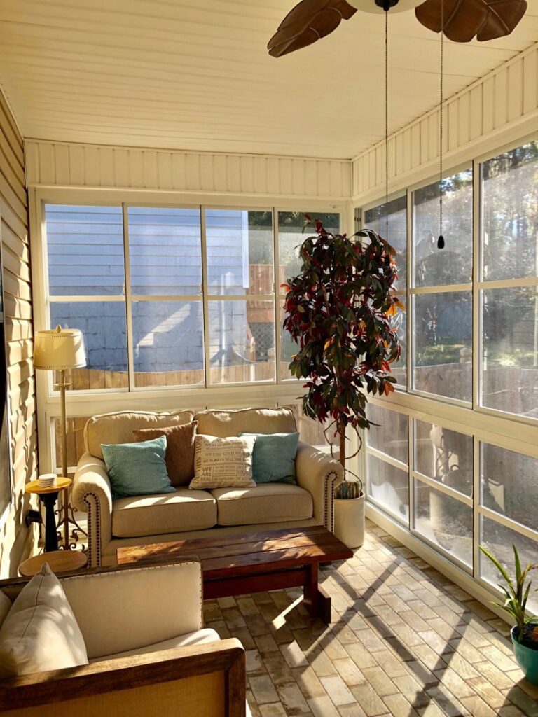 A cozy sunroom or enclosed patio with comfortable furniture and a ceiling fan, designed by NRG Industries in Tallahassee, FL.
