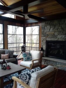 Finished sunroom interior featuring a stone fireplace, wooden ceiling, and seating area by Tschida Construction in Cologne, MN.