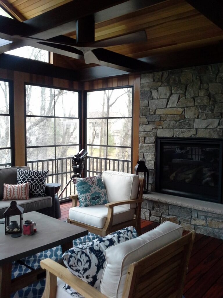 Finished sunroom interior featuring a stone fireplace, wooden ceiling, and seating area by Tschida Construction in Cologne, MN.
