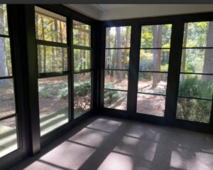 A cozy sunroom interior with dark window frames and a view of a wooded area, built by X-Terior Techs in Henrico, VA.