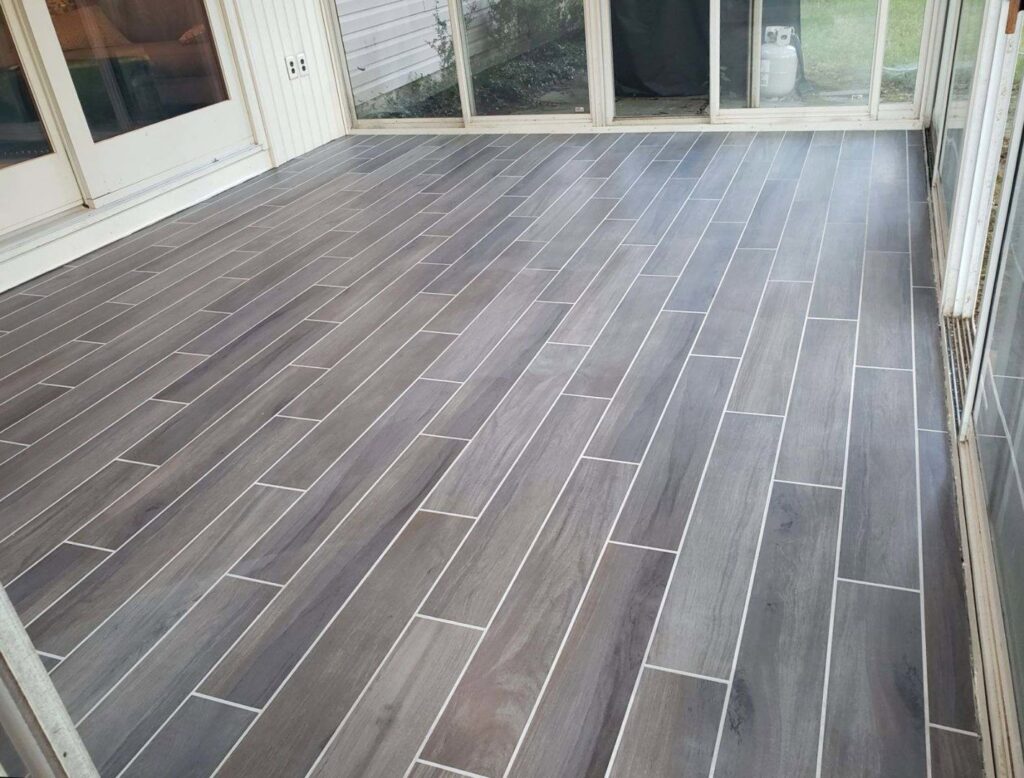 A newly installed wood-look tile floor in a sunroom or enclosed patio by Ace Tile & Finishing LLC, a general contractor in Philadelphia, PA.