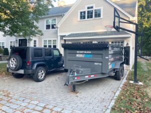 An SUV towing a Mobiledumps trailer in a residential driveway for junk removal in Rogers, AR.