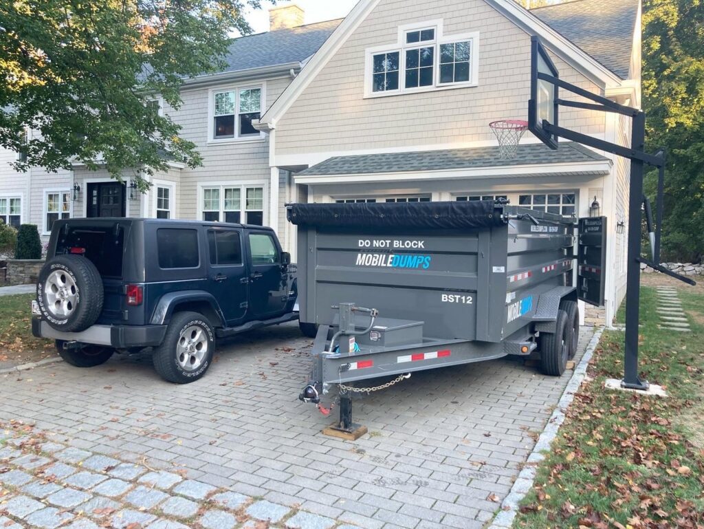 An SUV towing an empty Mobiledumps dumpster trailer in a residential driveway for Mobiledumps Northwest Arkansas in Rogers, AR.