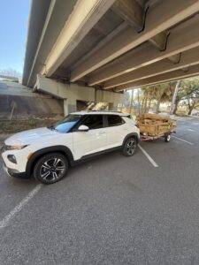 A white SUV towing a small trailer loaded with wooden debris, indicating a junk removal job by Reliable Pro in Tallahassee, FL.