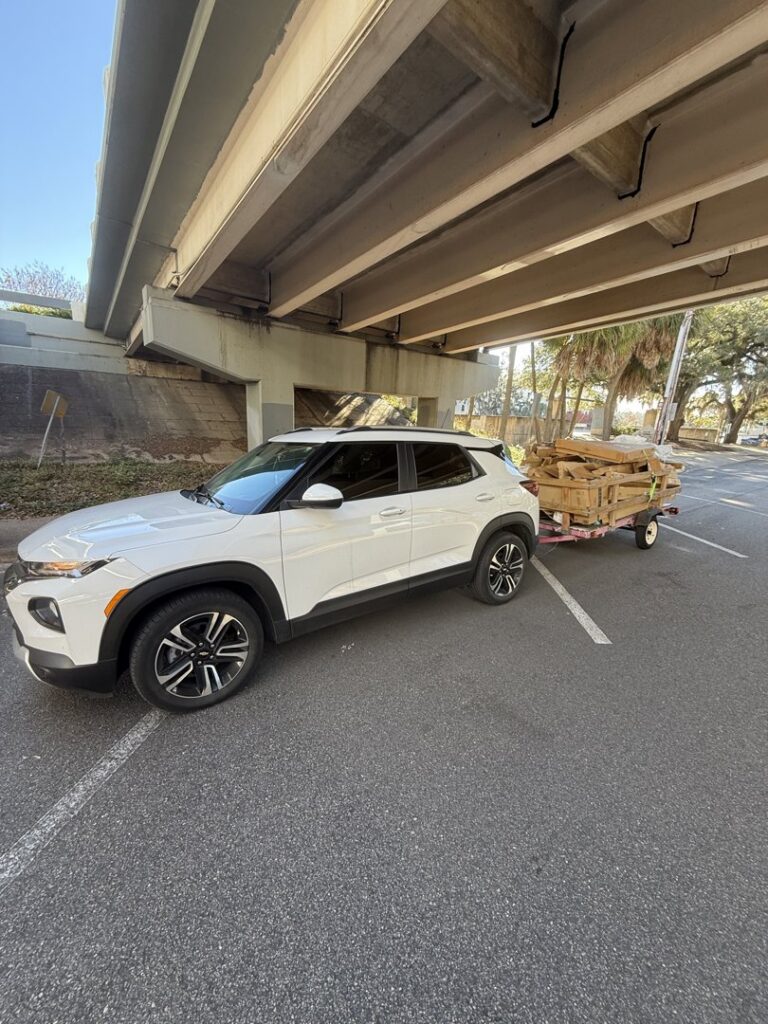 A white SUV towing a small trailer loaded with wooden debris, indicating a junk removal job by Reliable Pro in Tallahassee, FL.