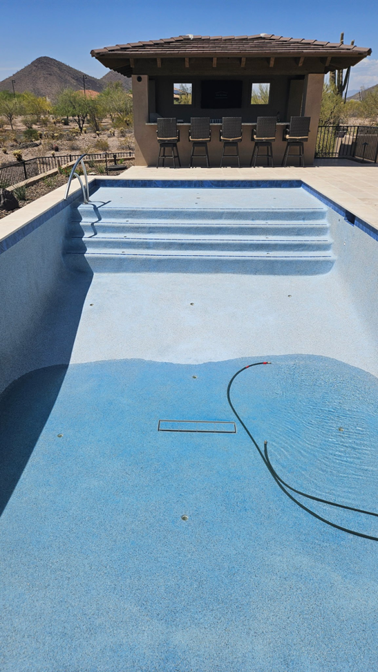 An empty swimming pool with a hose, ready for cleaning or repair by Unique Builders in Scottsdale, AZ.