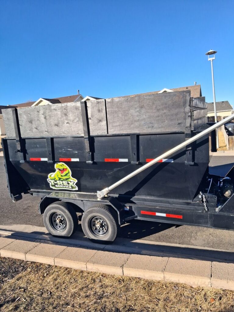 A black dump trailer with the T-Rex Service LLC logo, used for junk removal in Cheyenne, WY.