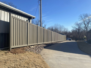 A tall brown privacy fence installed next to a residential building and driveway by Aaron Fence in Tulsa, OK.