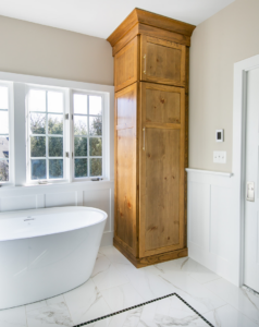 A tall custom wooden storage cabinet installed in a renovated bathroom by TCS Woodworking in Baltimore, MD